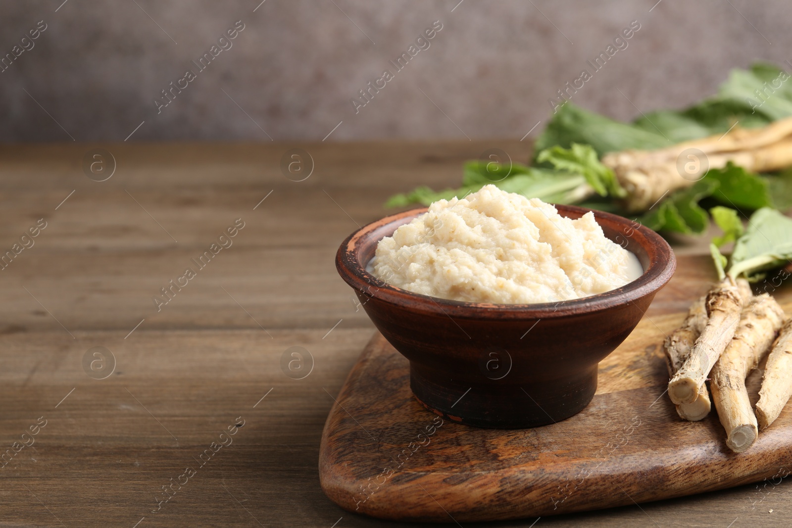 Photo of Tasty horseradish sauce and roots on wooden table, closeup. Space for text