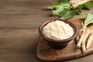 Photo of Tasty horseradish sauce and roots on wooden table, closeup. Space for text