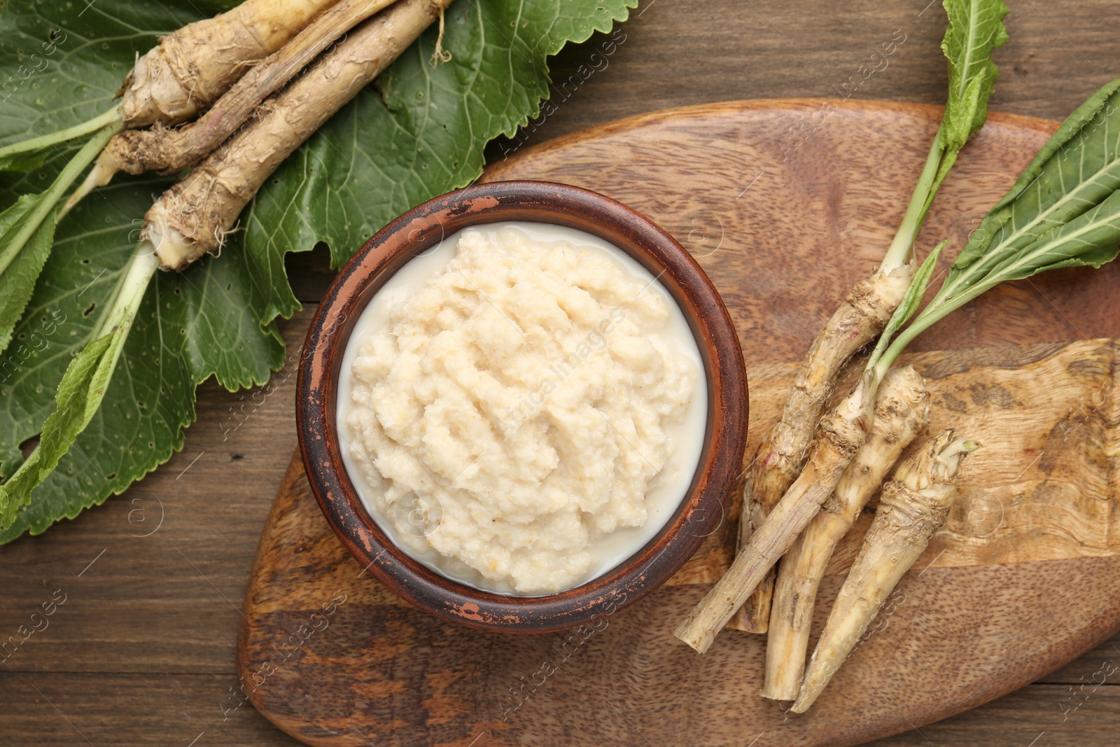Photo of Tasty horseradish sauce and roots on wooden table, flat lay