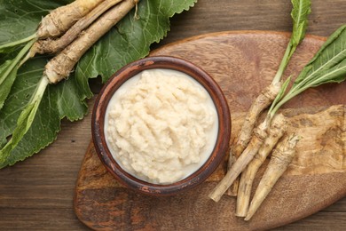 Photo of Tasty horseradish sauce and roots on wooden table, flat lay