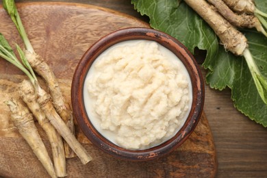 Photo of Tasty horseradish sauce and roots on wooden table, flat lay