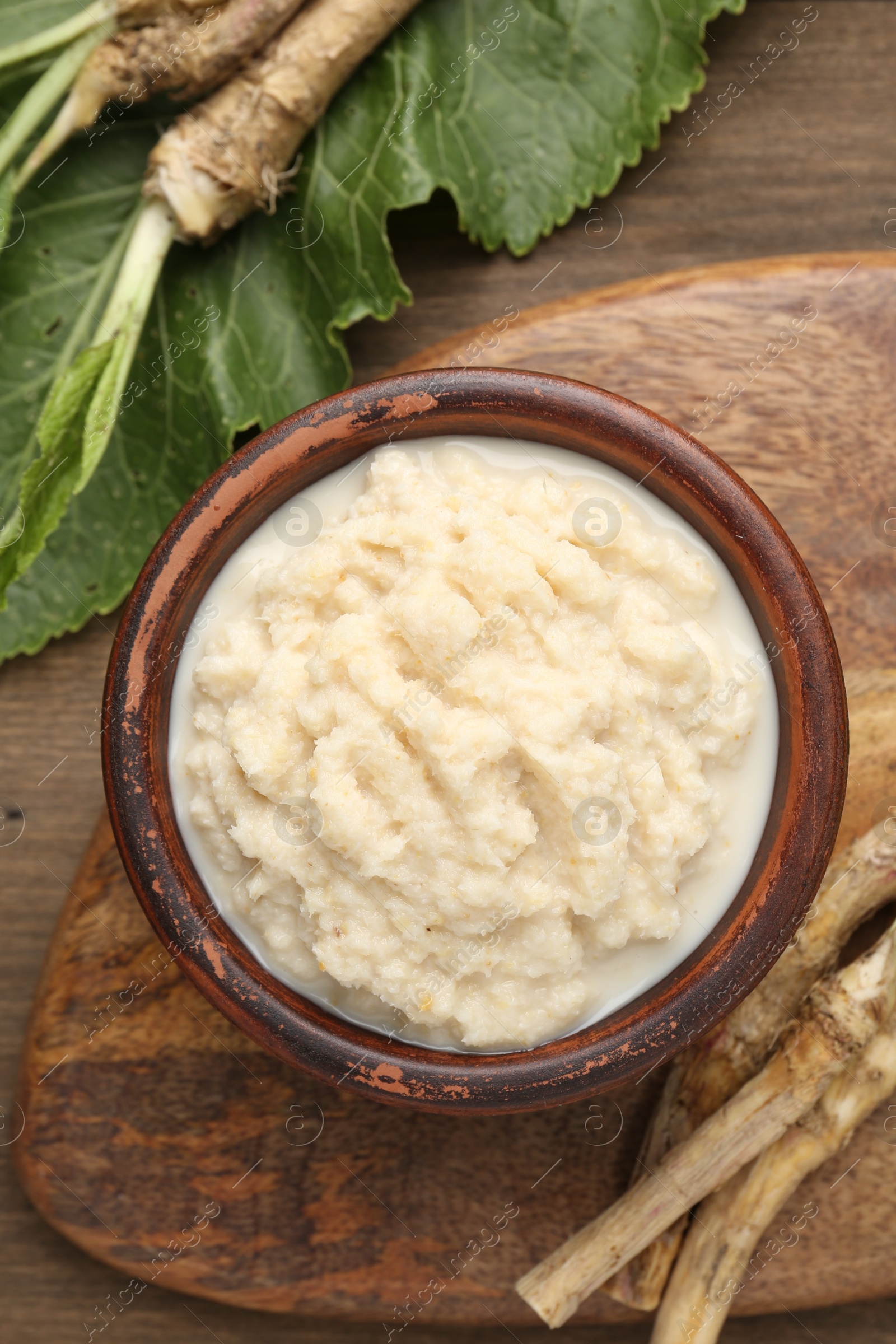 Photo of Tasty horseradish sauce and roots on wooden table, flat lay