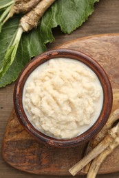 Photo of Tasty horseradish sauce and roots on wooden table, flat lay