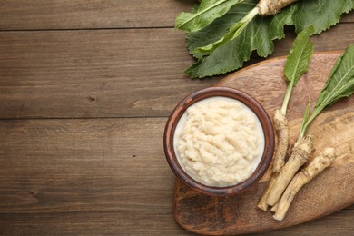Photo of Tasty horseradish sauce and roots on wooden table, flat lay. Space for text