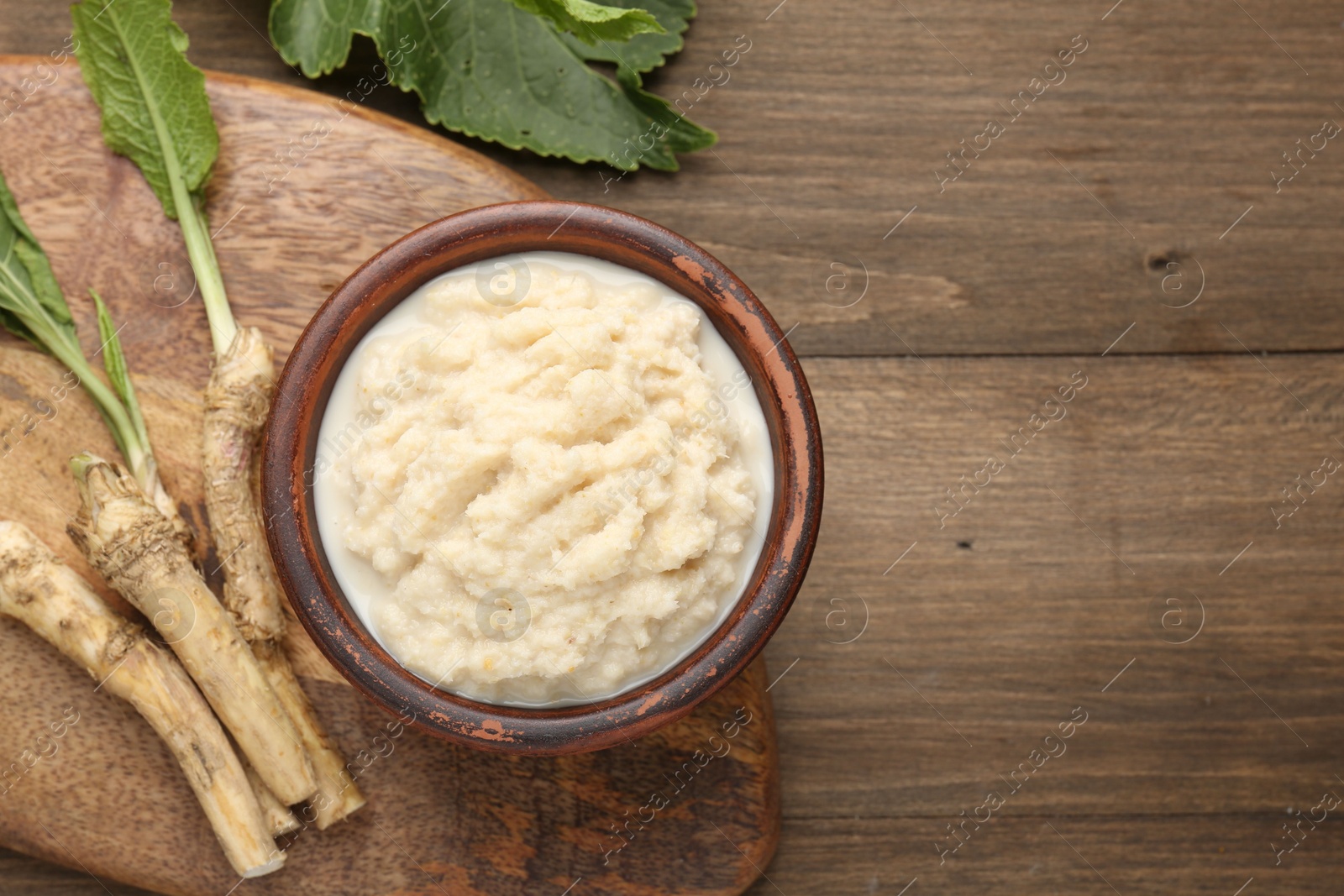 Photo of Tasty horseradish sauce and roots on wooden table, flat lay. Space for text