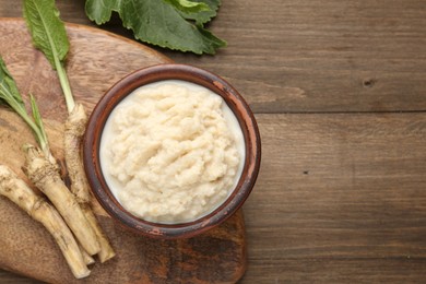 Photo of Tasty horseradish sauce and roots on wooden table, flat lay. Space for text