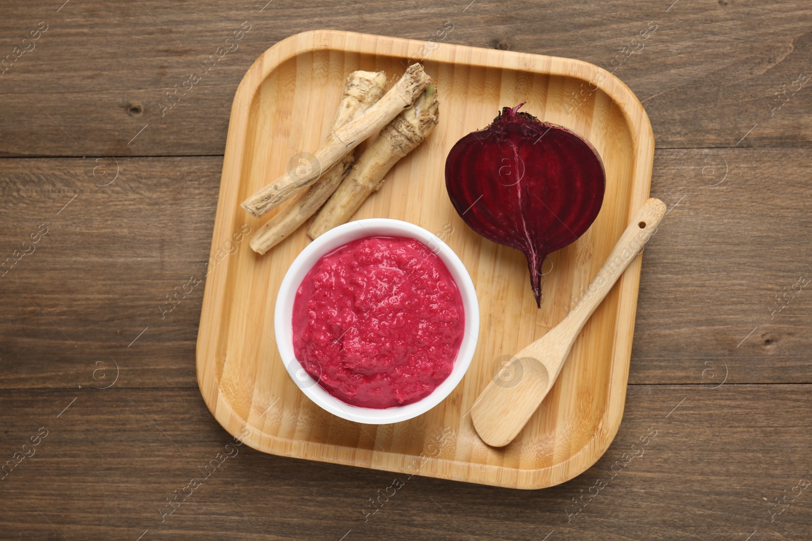 Photo of Tasty horseradish sauce with beetroot, spoon, roots and vegetable on wooden table, top view