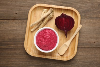 Photo of Tasty horseradish sauce with beetroot, spoon, roots and vegetable on wooden table, top view