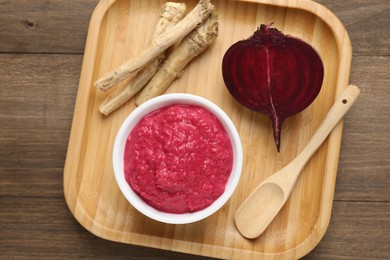Photo of Tasty horseradish sauce with beetroot, spoon, roots and vegetable on wooden table, top view