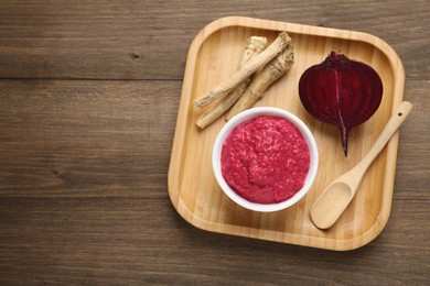 Photo of Tasty horseradish sauce with beetroot, spoon, roots and vegetable on wooden table, top view. Space for text