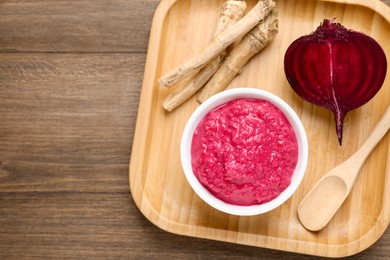 Photo of Tasty horseradish sauce with beetroot, spoon, roots and vegetable on wooden table, top view. Space for text