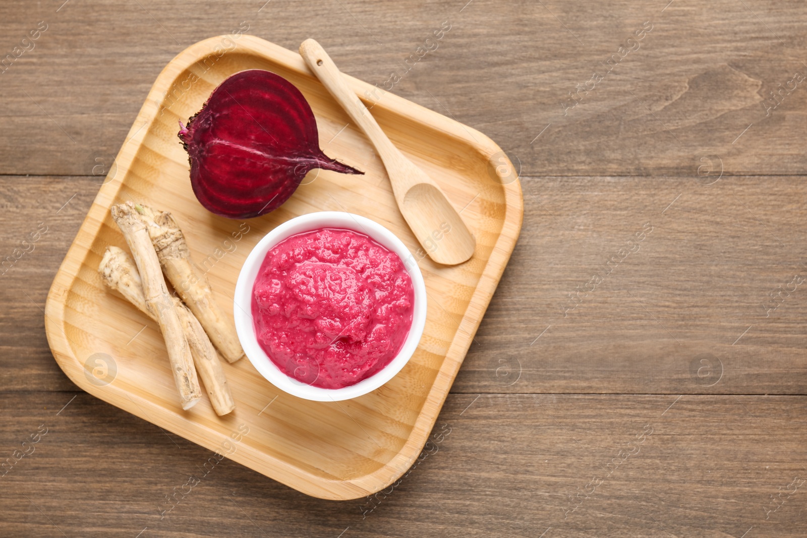Photo of Tasty horseradish sauce with beetroot, spoon, roots and vegetable on wooden table, top view. Space for text