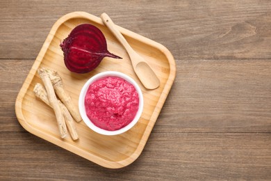 Photo of Tasty horseradish sauce with beetroot, spoon, roots and vegetable on wooden table, top view. Space for text