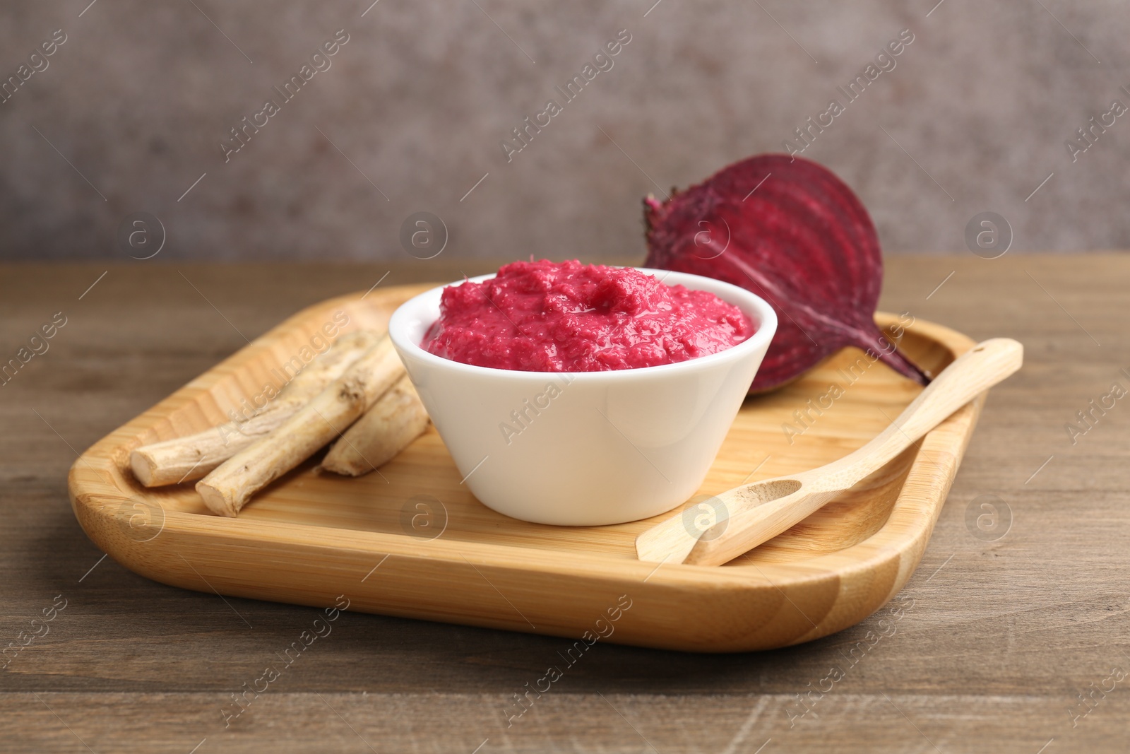 Photo of Tasty horseradish sauce with beetroot, spoon, roots and vegetable on wooden table, closeup
