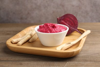 Photo of Tasty horseradish sauce with beetroot, spoon, roots and vegetable on wooden table, closeup