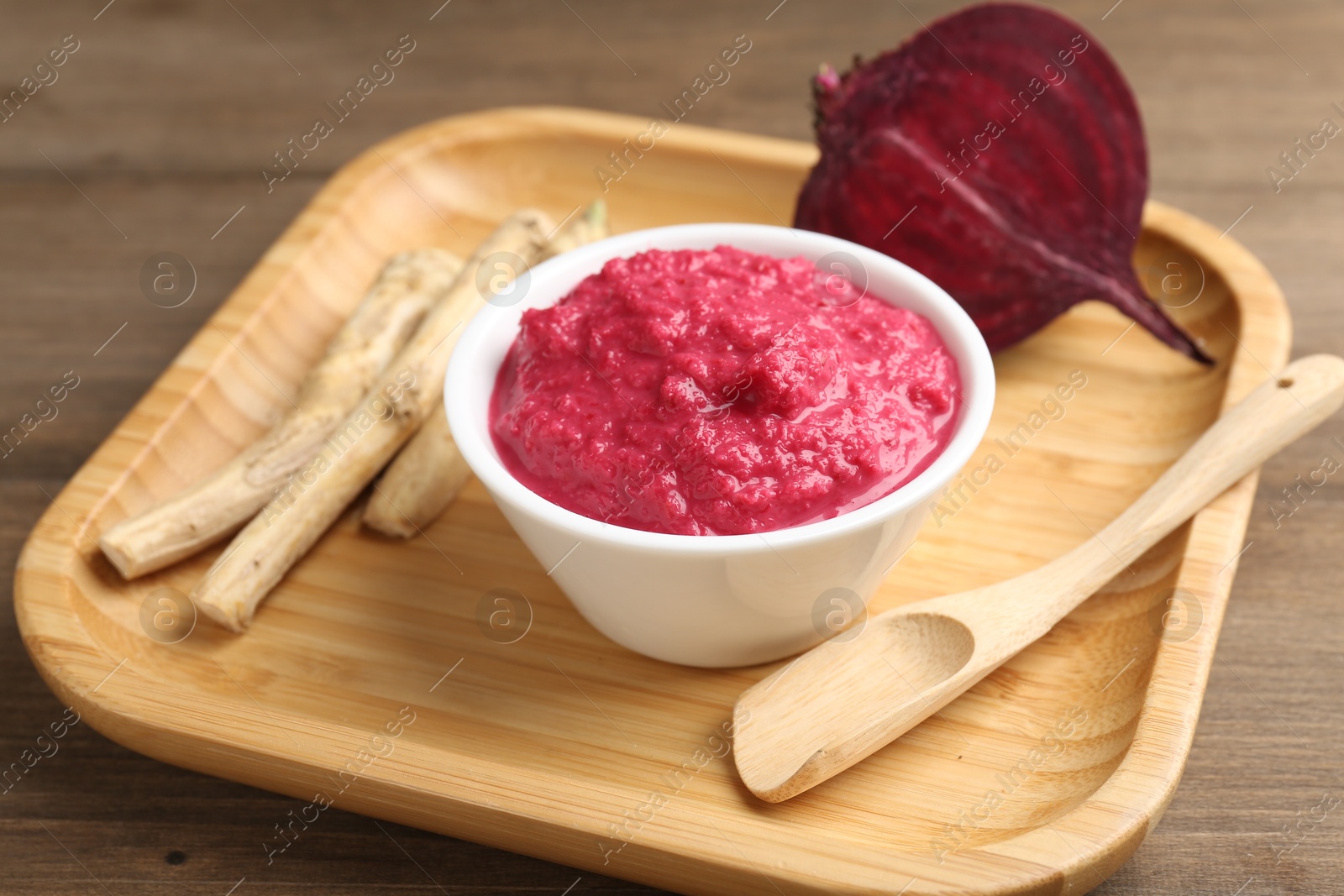 Photo of Tasty horseradish sauce with beetroot, spoon, roots and vegetable on wooden table, closeup