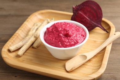 Photo of Tasty horseradish sauce with beetroot, spoon, roots and vegetable on wooden table, closeup