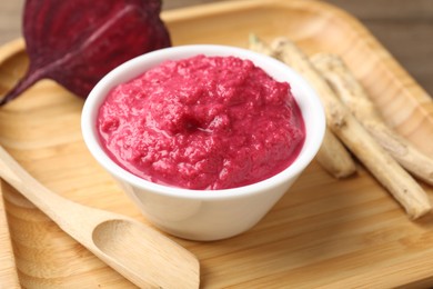 Photo of Tasty horseradish sauce with beetroot, spoon, roots and vegetable on wooden table, closeup