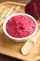 Photo of Tasty horseradish sauce with beetroot, spoon, roots and vegetable on wooden table, closeup