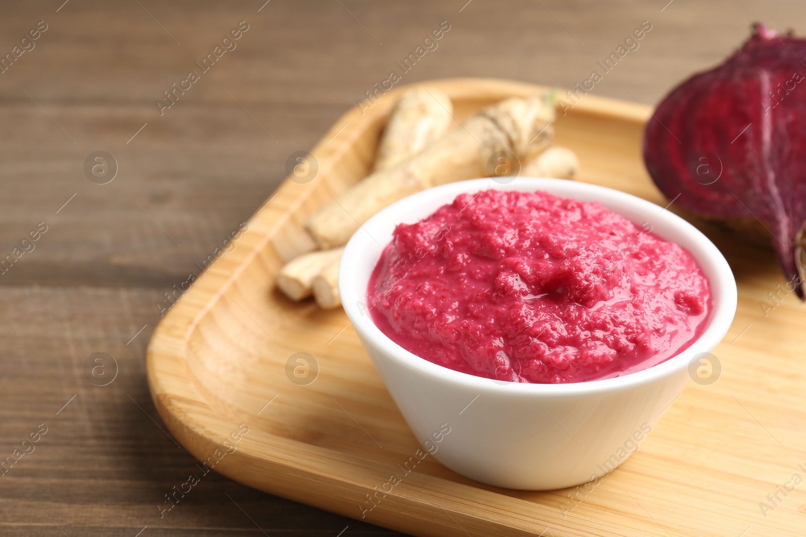 Photo of Tasty horseradish sauce with beetroot, roots and vegetable on wooden table, closeup