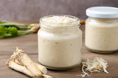 Photo of Tasty horseradish sauce and roots on wooden table, closeup