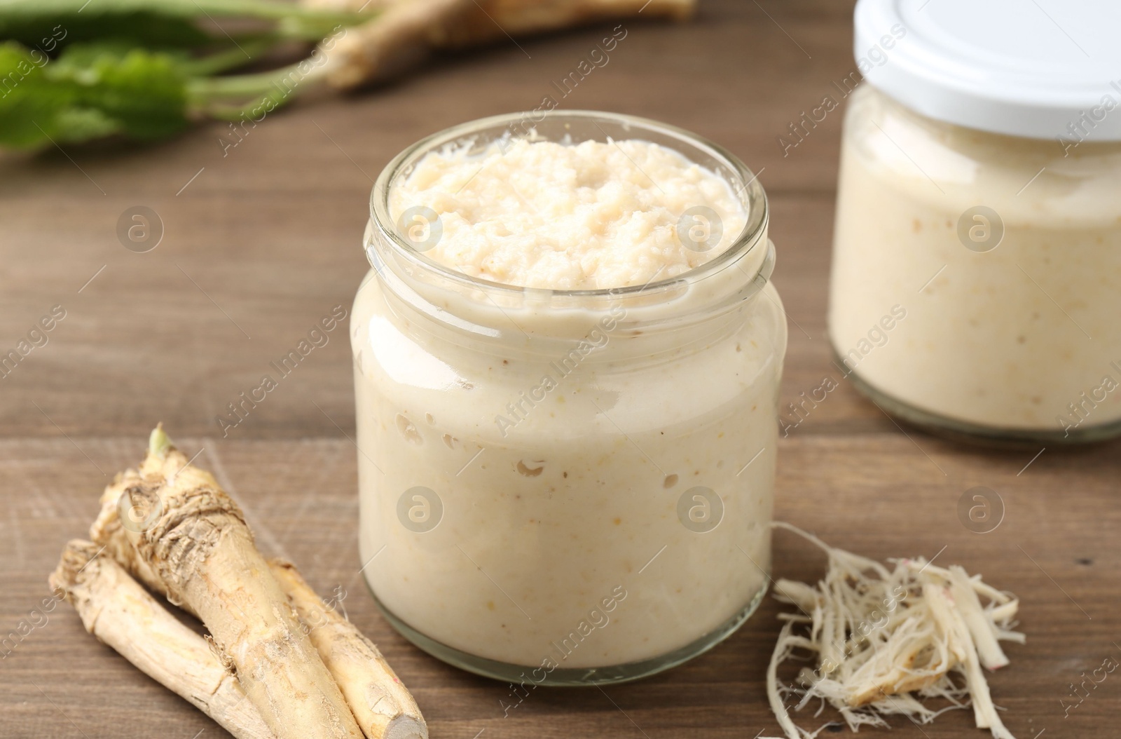 Photo of Tasty horseradish sauce and roots on wooden table, closeup