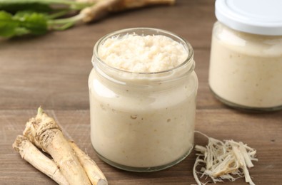 Photo of Tasty horseradish sauce and roots on wooden table, closeup
