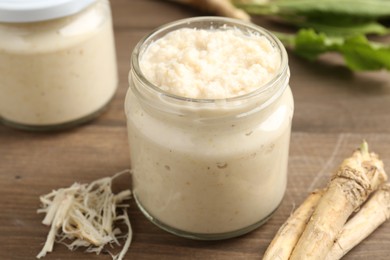 Photo of Tasty horseradish sauce and roots on wooden table, closeup