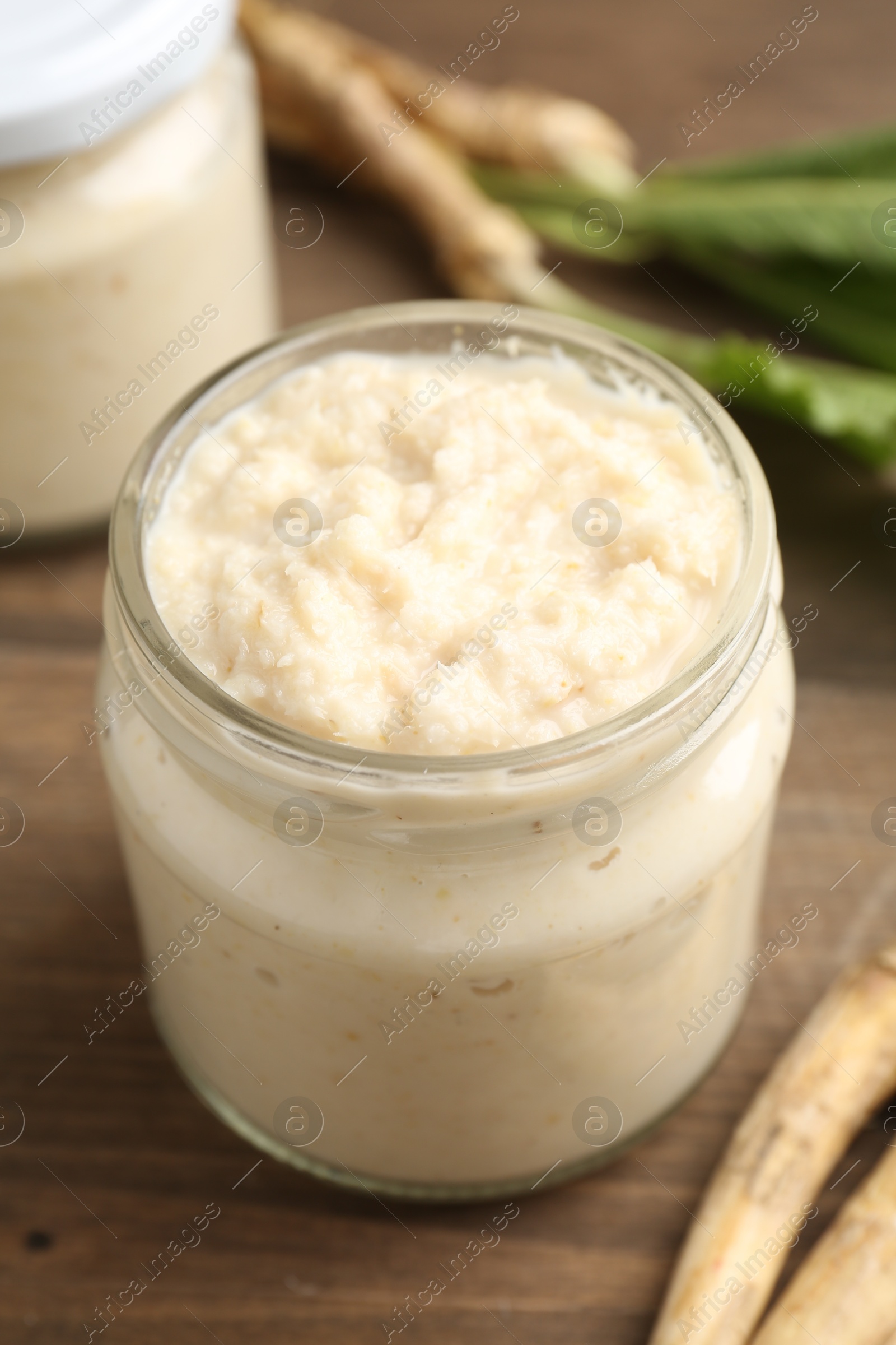 Photo of Tasty horseradish sauce and roots on wooden table, closeup