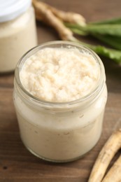 Photo of Tasty horseradish sauce and roots on wooden table, closeup