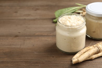 Photo of Tasty horseradish sauce and roots on wooden table, closeup. Space for text