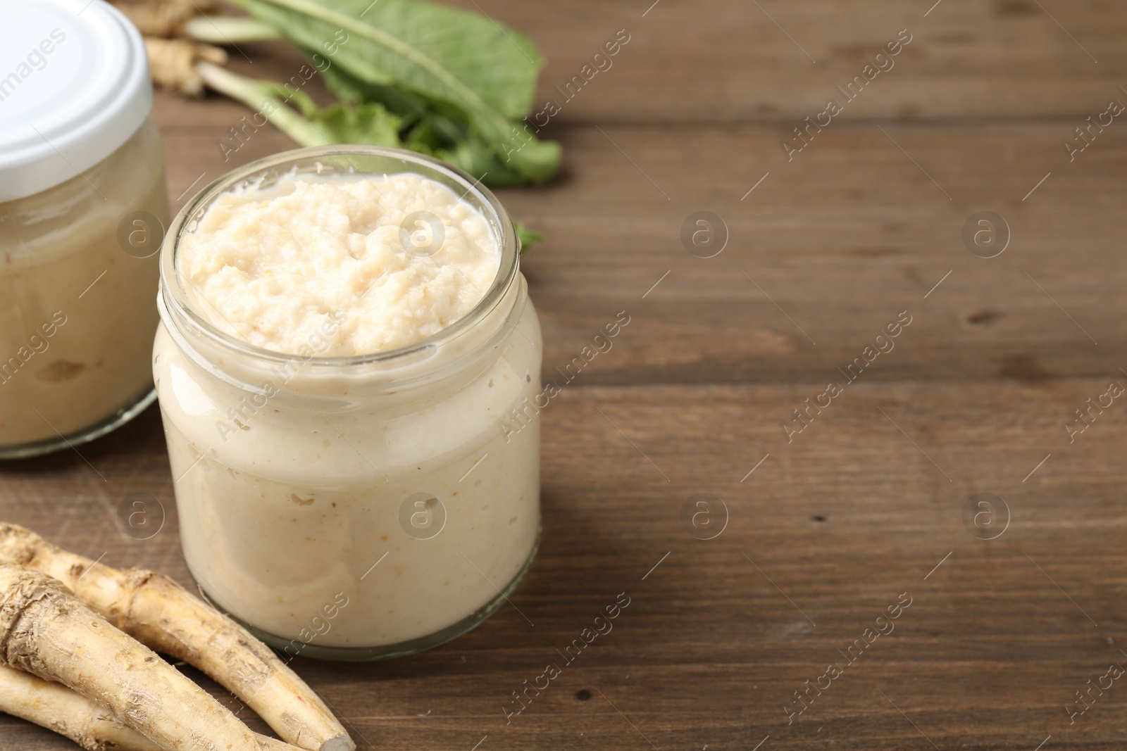 Photo of Tasty horseradish sauce and roots on wooden table, closeup. Space for text