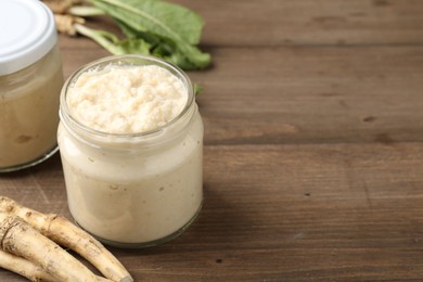 Photo of Tasty horseradish sauce and roots on wooden table, closeup. Space for text