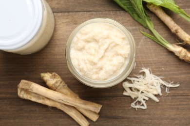 Photo of Tasty horseradish sauce and roots on wooden table, flat lay