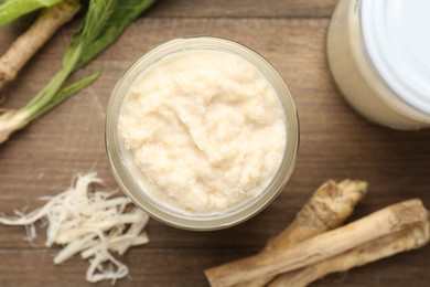 Photo of Tasty horseradish sauce and roots on wooden table, flat lay
