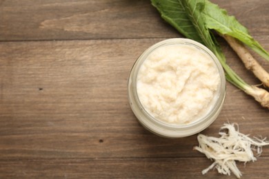 Photo of Tasty horseradish sauce and roots on wooden table, flat lay. Space for text