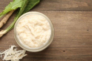 Photo of Tasty horseradish sauce and roots on wooden table, flat lay. Space for text