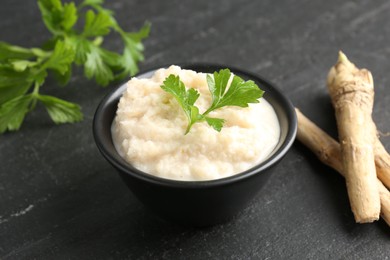 Photo of Tasty horseradish sauce with parsley and roots on black table, closeup