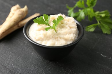 Photo of Tasty horseradish sauce with parsley and roots on black table, closeup