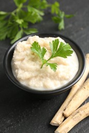 Photo of Tasty horseradish sauce with parsley and roots on black table, closeup