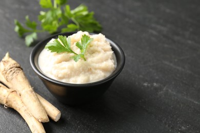 Photo of Tasty horseradish sauce with parsley and roots on black table, closeup. Space for text