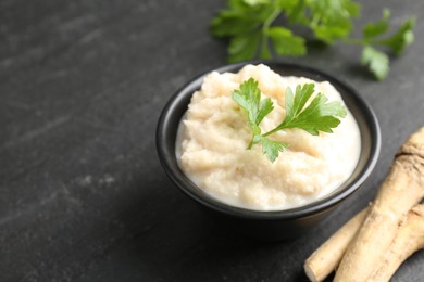 Photo of Tasty horseradish sauce with parsley and roots on black table, closeup. Space for text