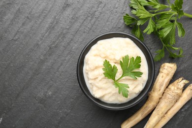 Photo of Tasty horseradish sauce with parsley and roots on black table, flat lay. Space for text