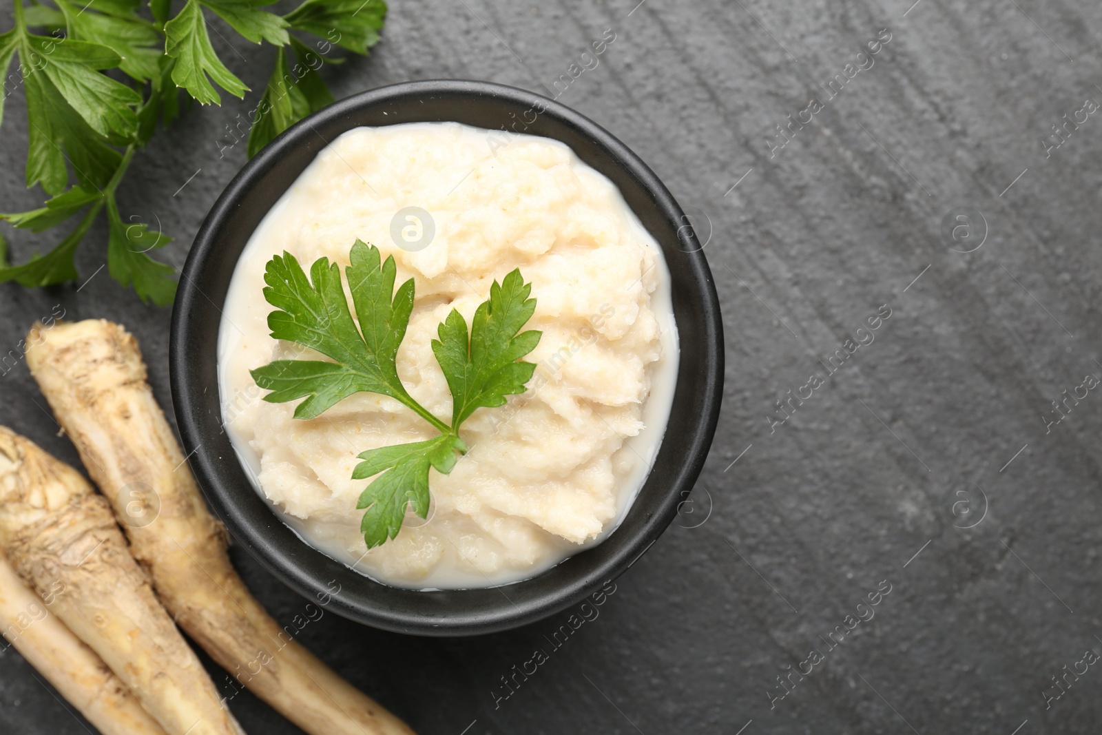 Photo of Tasty horseradish sauce with parsley and roots on black table, flat lay. Space for text