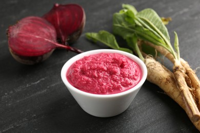 Photo of Tasty horseradish sauce with beetroot, roots and vegetable on black table, closeup