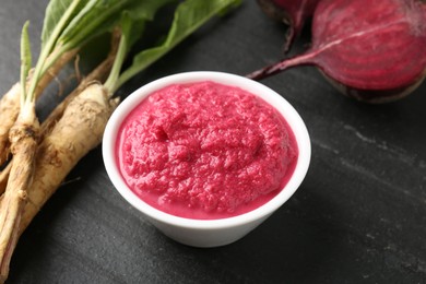 Photo of Tasty horseradish sauce with beetroot, roots and vegetable on black table, closeup
