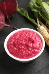 Photo of Tasty horseradish sauce with beetroot, roots and vegetable on black table, closeup