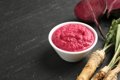 Photo of Tasty horseradish sauce with beetroot, roots and vegetable on black table, closeup. Space for text