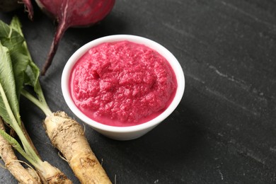 Photo of Tasty horseradish sauce with beetroot, roots and vegetable on black table, closeup. Space for text