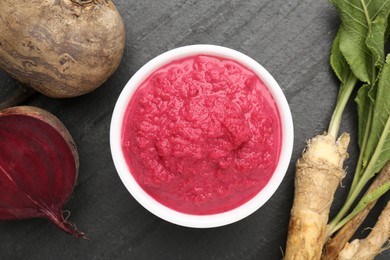 Photo of Tasty horseradish sauce with beetroot, roots and vegetable on black table, flat lay